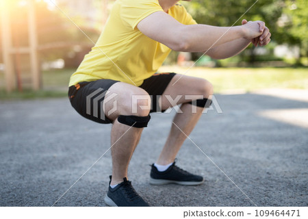 Man doing squat in knee support bandage during street workout Man doing squat in knee support bandage during street workout 109464471