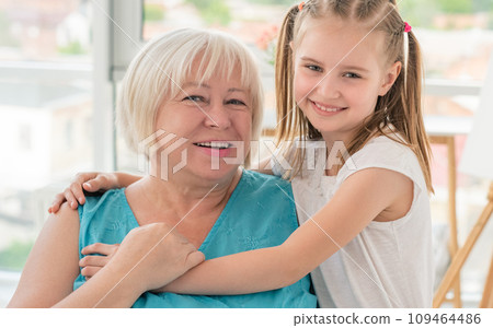 Portrait of happy grandmother hugging with little granddaughter indoors Portrait of happy grandmother hugging with little granddaughter indoors 109464486