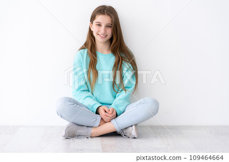 Pretty teenage girl sitting on floor leaning against white wall Pretty teenage girl sitting on floor leaning against white wall 109464664
