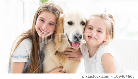 Portrait of smiling sisters with cute dog in bright room Portrait of smiling sisters with cute dog in bright room 109464665