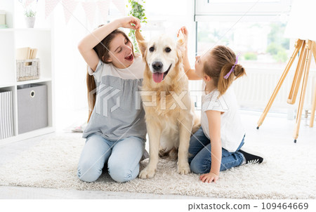 Cute sisters fooling with adorable dog's ears on floor at home Cute sisters fooling with adorable dog's ears on floor at home 109464669