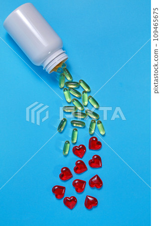 Omega-3 polyunsaturated fatty acids and red hearts pour out from a white plastic jar on a blue background. Prevention and treatment of atherosclerosis 109465675