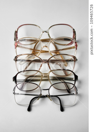 Old reading glasses stacked in a row on a white background Old reading glasses stacked in a row on a white background 109465726