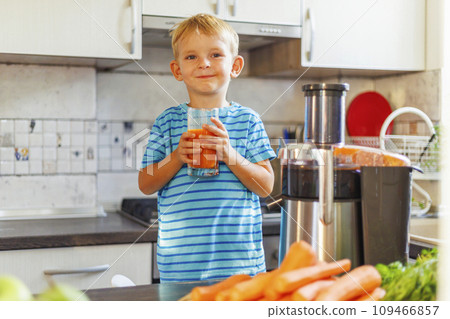 Little boy drinking freshly squeezed carrot juice from a glass in the kitchen 109466857