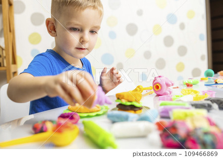Little boy enthusiastically plays with plasticine, play dough on white table 109466869