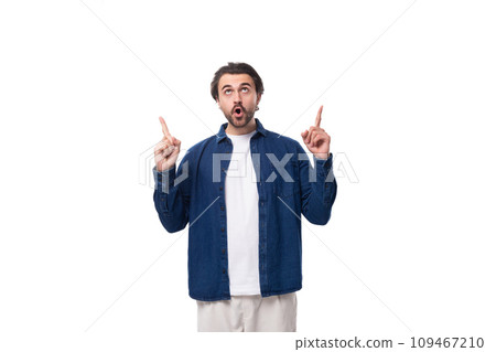 young handsome brunette european guy in a denim shirt shows his index finger up in surprise young handsome brunette european guy in a denim shirt shows his index finger up in surprise 109467210