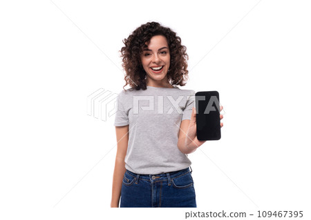 well-groomed caucasian young brunette woman with curly hair shows smartphone screen on white 109467395