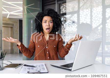 Upset businesswoman sitting at the table in the office, throwing her hands indignantly, confused by what happened, looking at the camera. 109467551