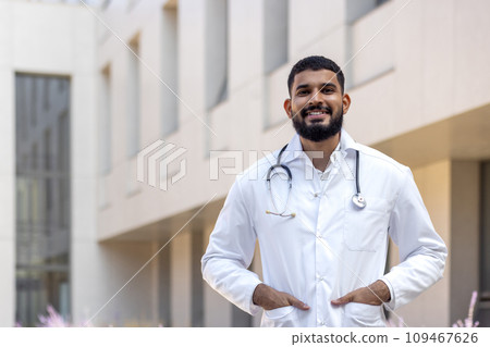 Portrait of a Latin American male doctor, nurse, veterinarian standing outside the clinic on the street in a white coat and smiling and confidently looking at the camera. 109467626