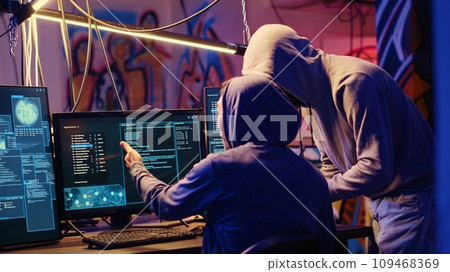 Evil cybercriminals in graffiti sprayed hideaway targeting vulnerable unpatched connections, discussing ways of getting past computer defenses and stealing valuable sensitive data 109468369