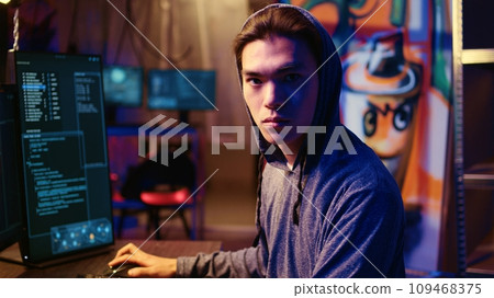 Portrait of asian hacker running code in graffiti painted basement, looking to find exploits for system vulnerabilities to be used against system owner for ransom, zoom in close up shot Portrait of asian hacker running code in graffiti painted basement, looking to find exploits for system vulnerabilities to be used against system owner for ransom, zoom in close up shot 109468375