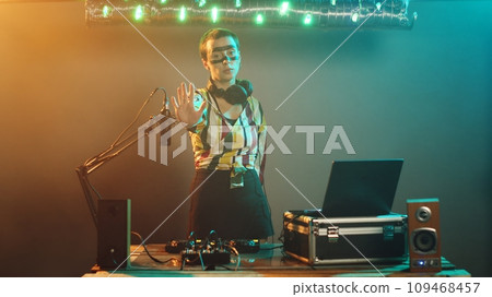 Crazy club musician raising palm to show denial and stop symbol on stage, mixing modern techno sounds on DJ turntables. Performer using audio stereo instruments, adjusting buttons. Tripod shot. 109468457