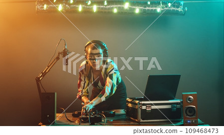 Woman artist mixing techno songs on audio buttons, having fun with turntables playing modern music at nightclub party. Young performer testing bass control key, adjust volume. Tripod shot. 109468473
