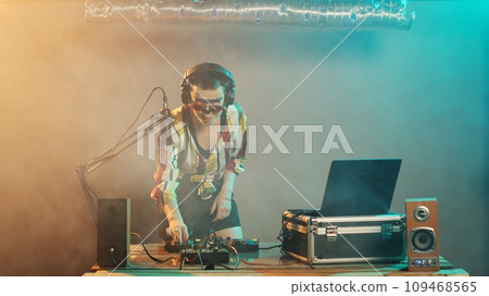 Female musician sticking tongue out and acting crazy, making silly faces and fooling around on nightclub stage. Confident cool disc jockey using turntables and microphone, mixing music. 109468565
