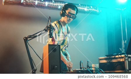 DJ artist using clubbing mixing turntables at party to play remix music at techno event, working with audio instruments at nightclub. Playing stereo sounds with bass electronics. Handheld shot. DJ artist using clubbing mixing turntables at party to play remix music at techno event, working with audio instruments at nightclub. Playing stereo sounds with bass electronics. Handheld shot. 109468568