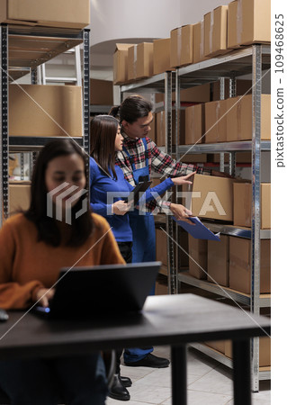 Postal storehouse employees managing order picking and shipping operation. Postal warehouse asian coworkers taking cardboard box from shelf and analyzing product checklist on digital tablet Postal storehouse employees managing order picking and shipping operation. Postal warehouse asian coworkers taking cardboard box from shelf and analyzing product checklist on digital tablet 109468625