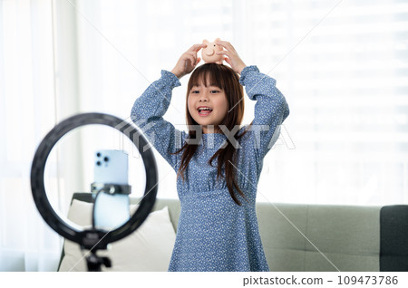 A cute young Asian girl is reviewing her toy while live streaming on her social media. 109473786