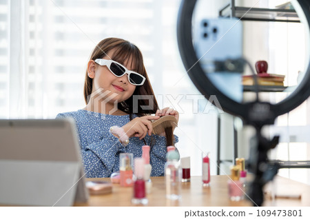 A cute young Asian girl kid influencer is combing her hair while recording her makeup tutorial video A cute young Asian girl kid influencer is combing her hair while recording her makeup tutorial video 109473801