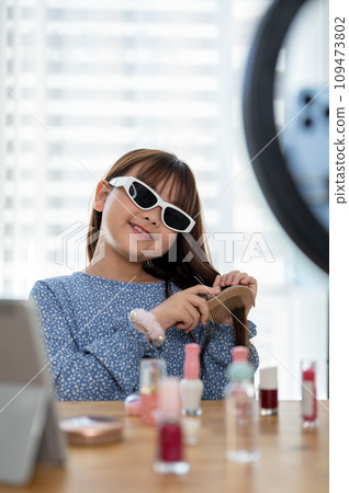 A cute young Asian girl kid influencer is combing her hair while recording her makeup tutorial video 109473802