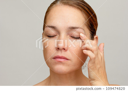 Middle aged caucasian woman of 40s with closed eyes holding finger on eyelid to show eyes aging Middle aged caucasian woman of 40s with closed eyes holding finger on eyelid to show eyes aging 109474820