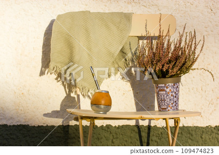 Mate calabash with bombilla. Healthy infused drink, classic Yerba mate tea on a chair on a cozy patio, backyard. Hot beverage on a terrace. Traditional Latin America cuisine. Useful drink still life. 109474823