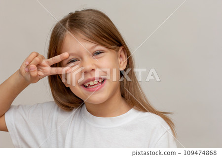 Portrait of caucasian happy little girl with open wide smile making v sign near eyes looking at camera 109474868