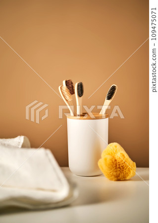Bamboo toothbrushes in a cup and a towel in a bathroom interior. 109475071