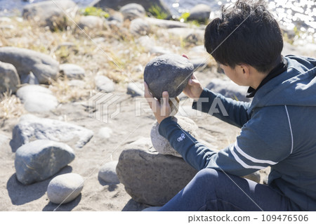 A man doing rock balancing on the riverbank 109476506