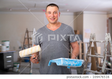 Portrait of positive man with paint roller and tray 109476516