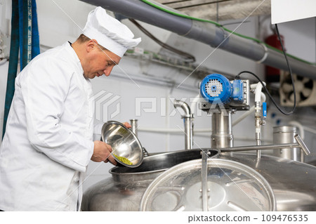 Brewmaster pouring hop pellets from bowl into beer production fermenter Brewmaster pouring hop pellets from bowl into beer production fermenter 109476535