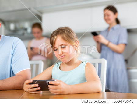Interested tween girl playing online game on smartphone at table Interested tween girl playing online game on smartphone at table 109476543