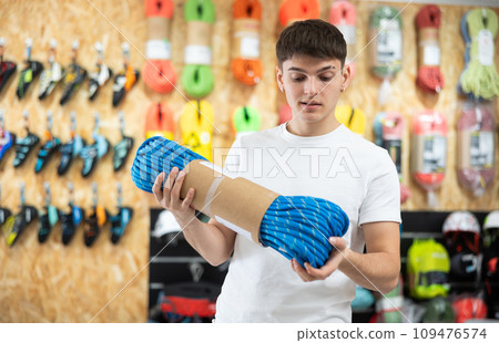Young guy carefully selects climbing rope for a hike in sports equipment store Young guy carefully selects climbing rope for a hike in sports equipment store 109476574