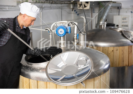 Beer factory worker mixing beer in tank Beer factory worker mixing beer in tank 109476628