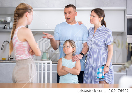 Disgruntled parents reprimanding eldest teenage girl in home kitchen 109476632