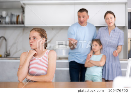 Upset teenage girl listening to disgruntled parents reprimanding her 109476790
