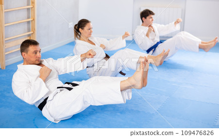 Woman and men in kimono train abdominal muscles and do punches at same time during karate or judo training 109476826