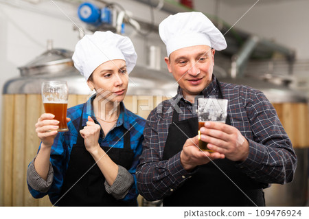 Interested male and female brewers examining quality of beer in brewery 109476924