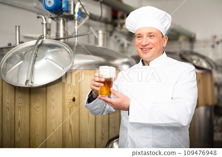 Portrait of brewer who is standing with glass of beer on his workplace in brew-house 109476948