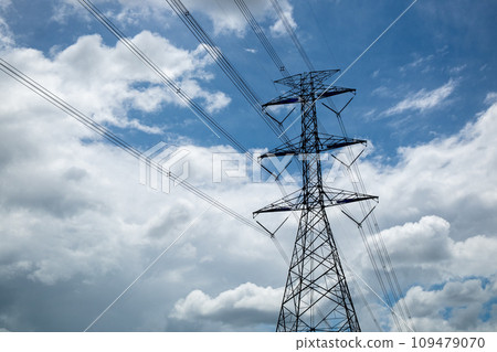 High-Voltage Electric Poles Standing Against a Backdrop of a Beautiful Blue Sky and Clouds. 109479070