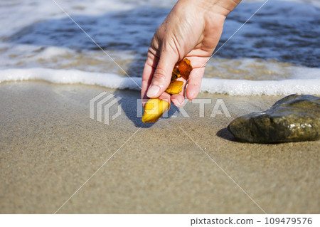 Beautiful pieces of amber in the hand of the sea background. A glowing wavy piece of amber in the palm of your hand. The sunstone. Beautiful pieces of amber in the hand of the sea background. A glowing wavy piece of amber in the palm of your hand. The sunstone. 109479576