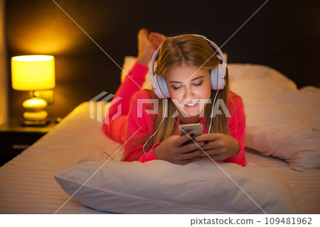 Young women listening to the music from smartphone on bed Young women listening to the music from smartphone on bed 109481962