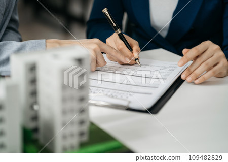 Real estate broker agent presenting and consult to customer to decision making sign insurance form agreement, home model, concerning mortgage loan offer in office. 109482829