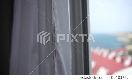 Sea view through the window with white transparent curtains slowly swaying in the wind. Resort, apartment with sea view. Leisure, relax, beauty, travel. 109483262