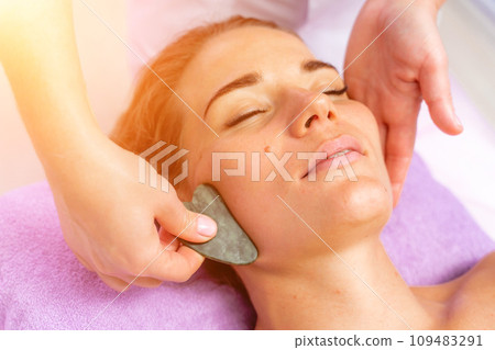 Relaxing massage. European woman getting quartz guache face massage in spa salon, side view 109483291