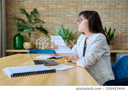Serious mature businesswoman reading official letter, sitting in office 109483444