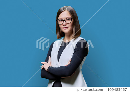 Young confident woman with crossed arms looking at camera on blue background Young confident woman with crossed arms looking at camera on blue background 109483467