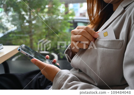 Cropped shot businesswoman using mobile phone and picking credit card from suit pocket 109484048