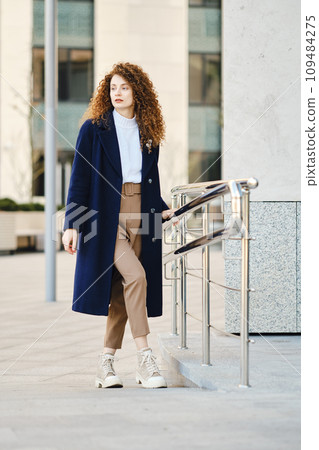Young woman in wool coat posing near modern building 109484275