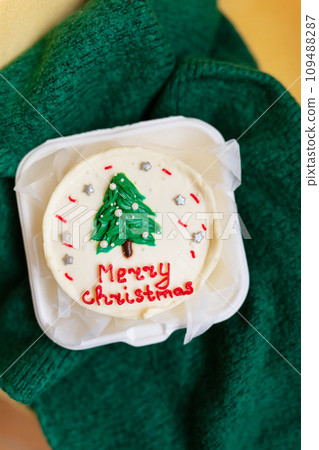 A festive Christmas cupcake with a green tree and red Merry Christmas text on a white frosting. 109488287