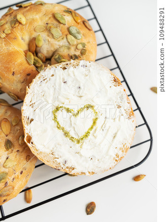 Round bread with cream cheese and a heart made of pesto on a white background. Round bread with cream cheese and a heart made of pesto on a white background. 109488291